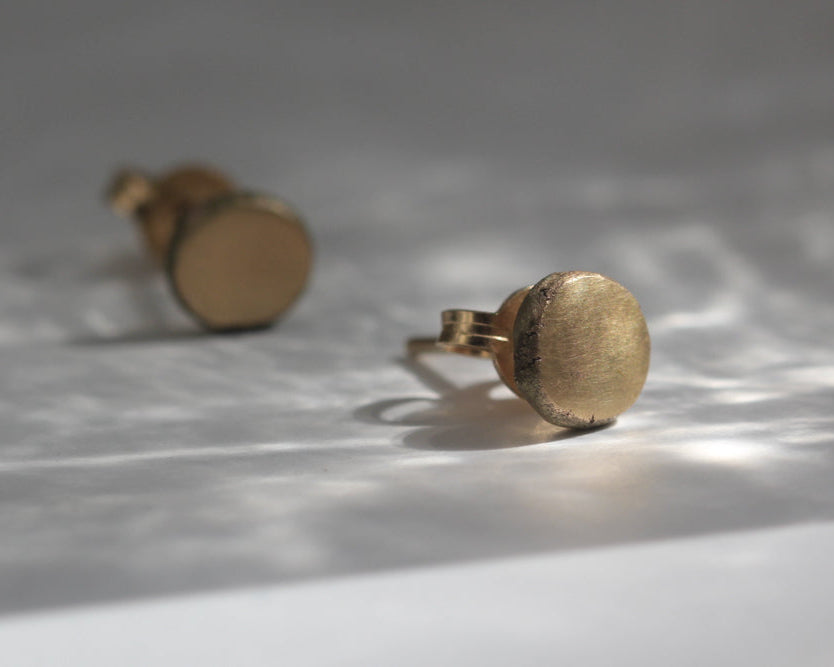 Pair of gold stud earrings on a reflective surface